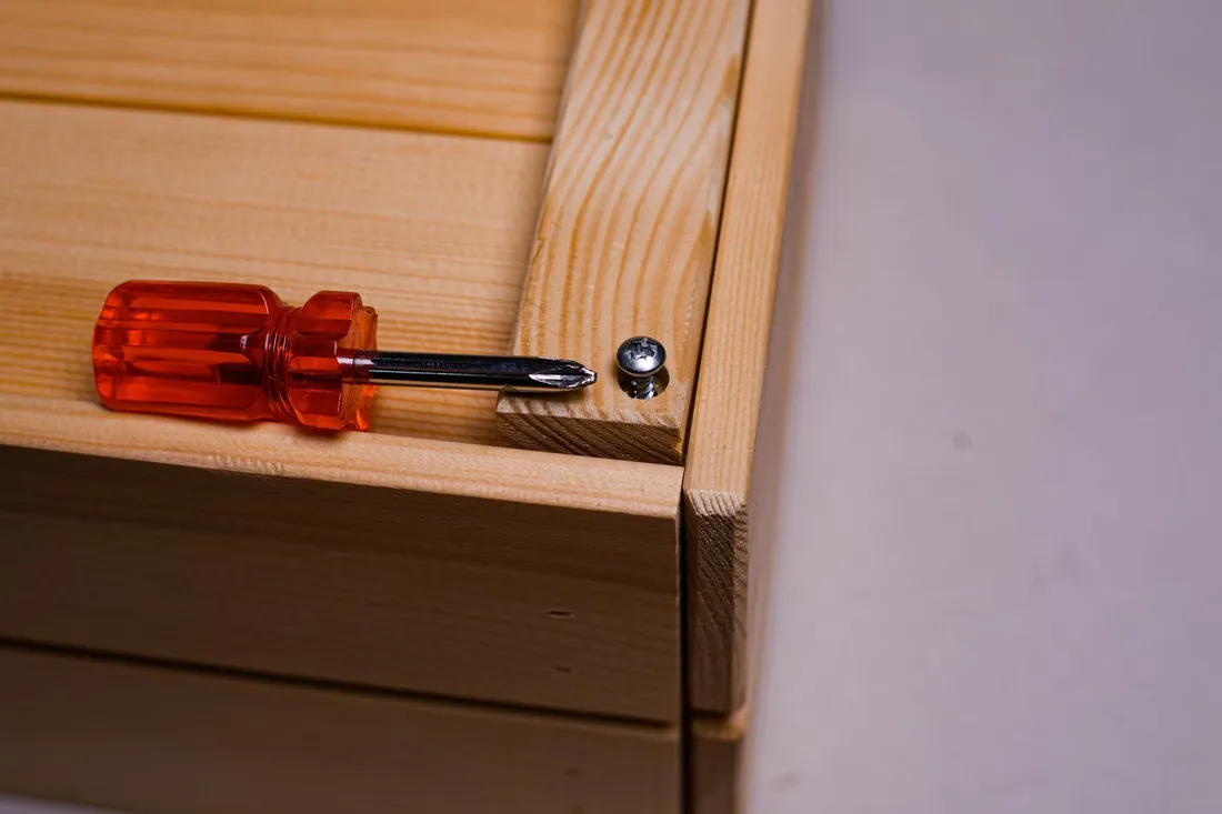 Schraubendreher und Schraube auf unlackiertem Holz, wie beim Zerlegen und Neusetzen einer Küchenzeile
