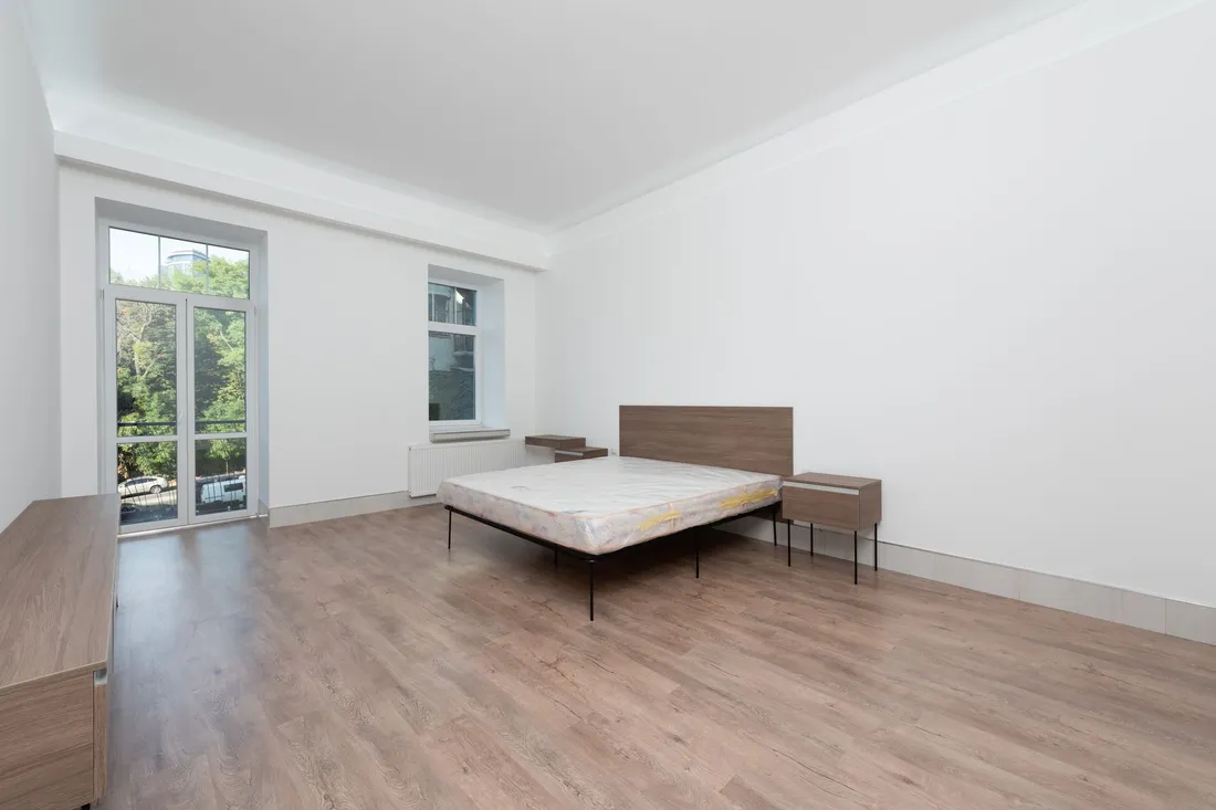Nackte Matratze auf einem schlichten Bettgestell mit Nachttisch in einem fast leeren Zimmer